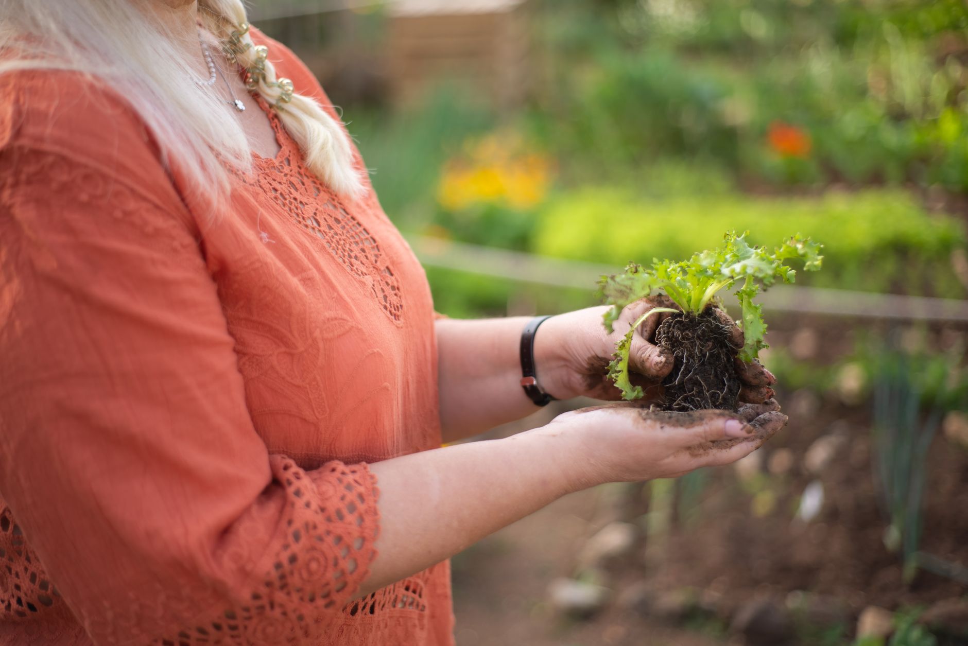 Woman holding a plant seedling in a garden, symbolizing growth and nature.